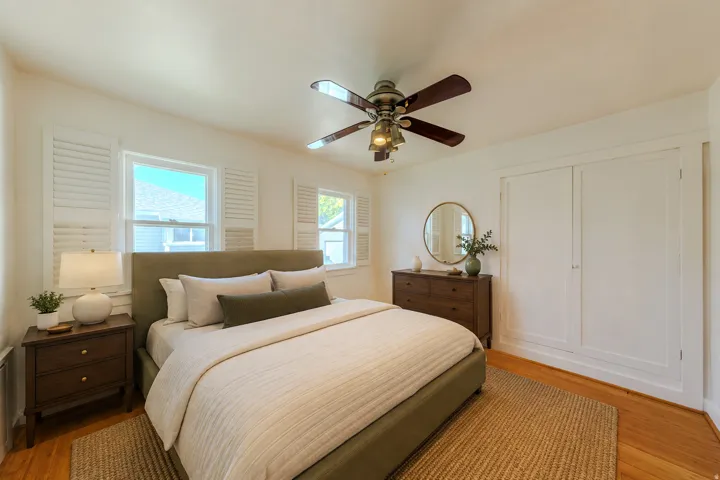Hardwood flooring, painted white walls, two windows with white plantation shutters, built-in closet with white doors, and a ceiling fan with integrated lighting