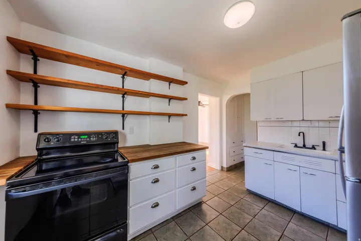 White shaker cabinetry, wood-finish countertops, black electric range, white subway tile backsplash, and tile flooring