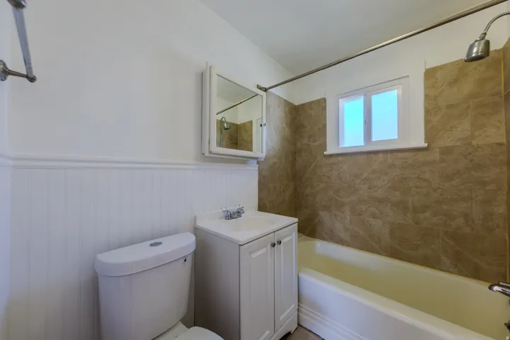 Bathroom featuring white wainscoting, a wall-mounted medicine cabinet, a vanity with a built-in sink, and a shower/tub combination with tile surround