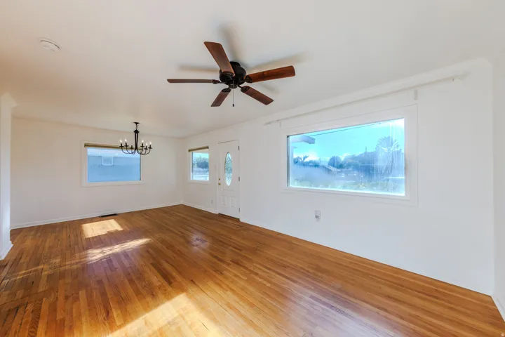 Hardwood flooring, white walls, ceiling fan, decorative chandelier, and a front entry door with an oval glass insert