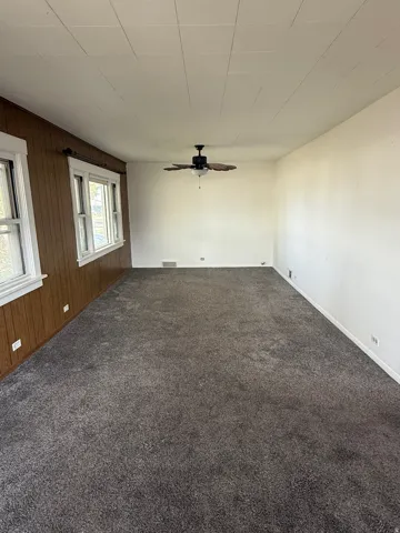 Spacious room featuring gray carpeting, white walls, and a ceiling fan