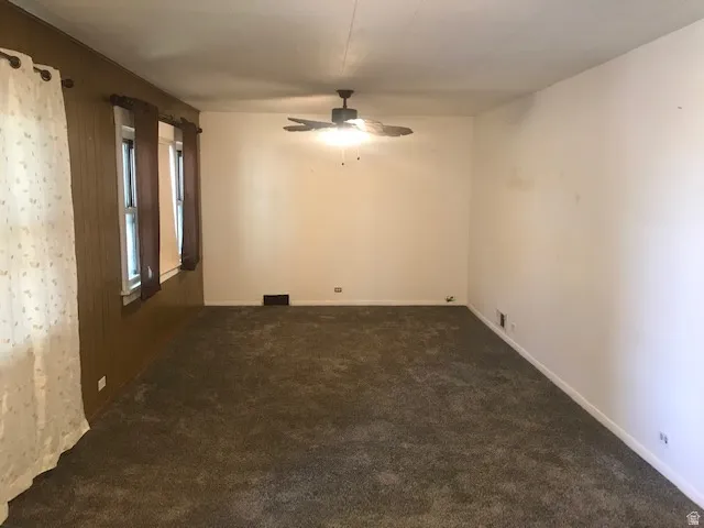 Expansive carpeted area with a ceiling fan light fixture and multiple windows
