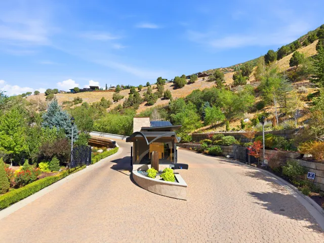 Paved driveway with a modern architectural entrance feature, surrounded by mature landscaping and natural hillside