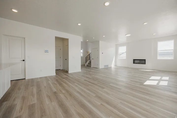 Spacious open-concept room featuring light wood-finish flooring, recessed lighting, and a built-in fireplace
