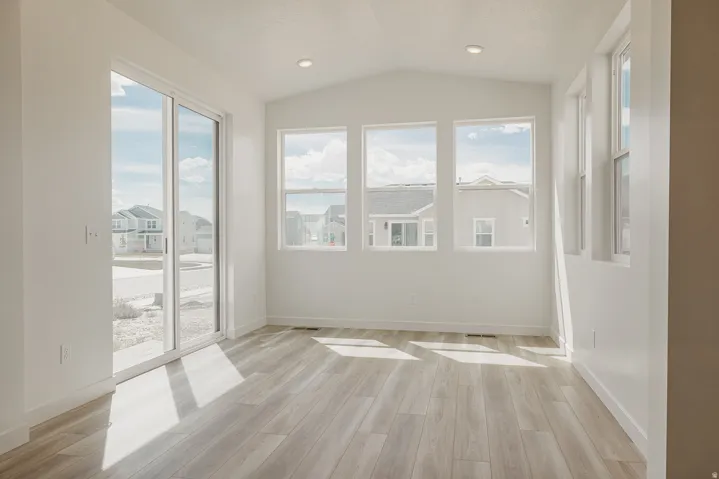 Vaulted ceiling, recessed lighting, wood-finish flooring, multiple windows, and a sliding glass door