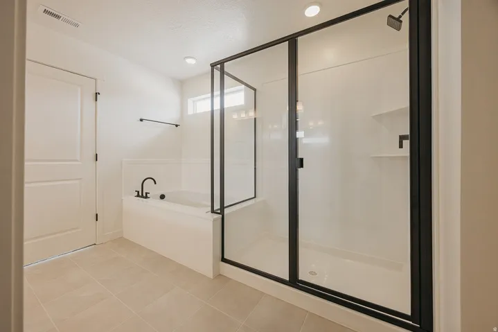 Tiled flooring, built-in bathtub with matte black fixtures, glass-enclosed shower with matte black frame, recessed lighting, and a transom window