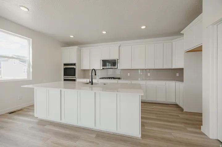 Spacious kitchen featuring an expansive island, white cabinetry, integrated double ovens, a gas range, and wood-finish flooring