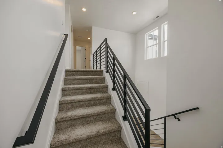 Carpeted staircase featuring black metal railings and white walls