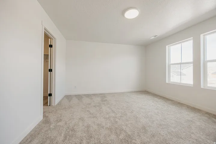Bright room featuring two windows, neutral carpeting, a ceiling-mounted light fixture, and a white interior door with black hardware