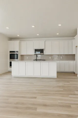 Modern kitchen featuring white shaker cabinetry, an island with countertop, stainless steel appliances, a tile backsplash, and wood-finish flooring
