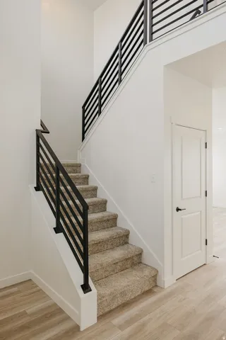 Staircase with horizontal metal railings, carpeted treads, and light wood-finish flooring