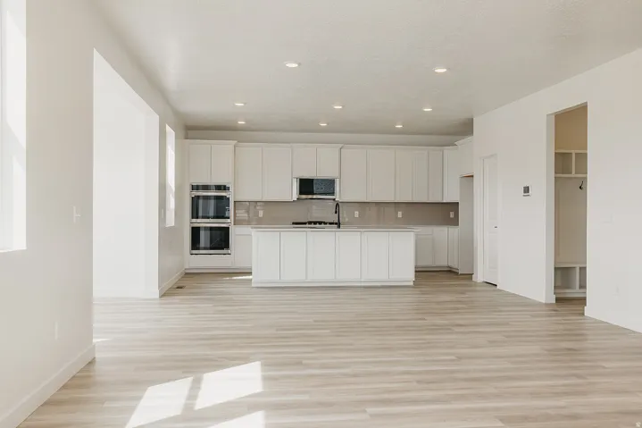 Open-concept kitchen with white cabinetry, stainless steel double wall ovens, and an island with a gas range