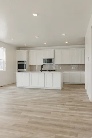 Kitchen featuring white cabinetry, built-in double ovens, a central island with a gas range, a dark faucet, and wood-finish flooring