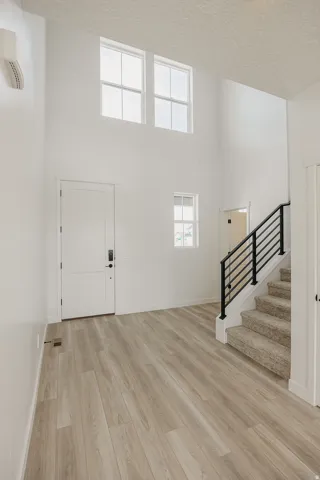 Wood-finish flooring throughout, complemented by a white entry door, and a staircase featuring a black metal railing