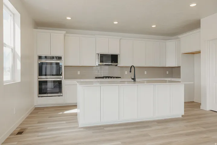 Kitchen featuring a spacious island, built-in double ovens, light-finish wood flooring, white cabinetry, and recessed lighting