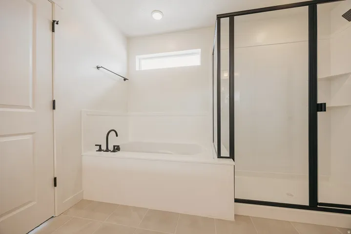 Integrated soaking tub with matte black fixtures, separate shower with black-framed glass enclosure, and tiled flooring