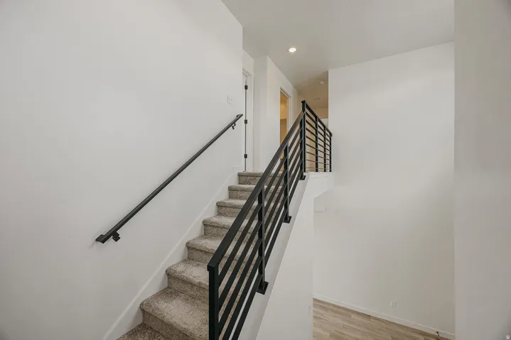 Carpeted staircase with black metal handrails and white walls