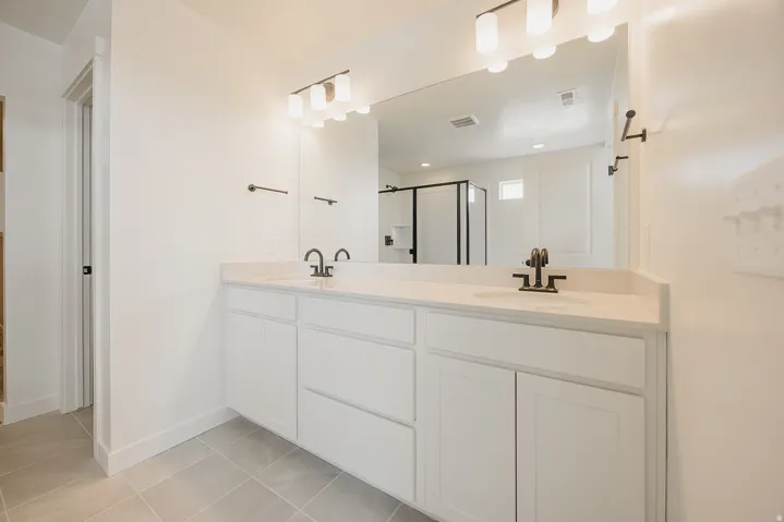 Dual vanity with integrated sinks, white cabinetry, a large wall mirror, and modern bronze-finish fixtures