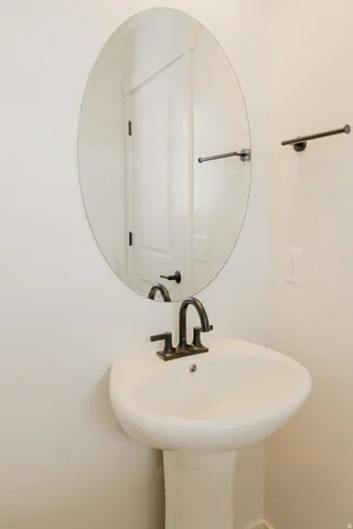 Pedestal sink with a dark bronze faucet, oval wall mirror, and dark bronze towel bar