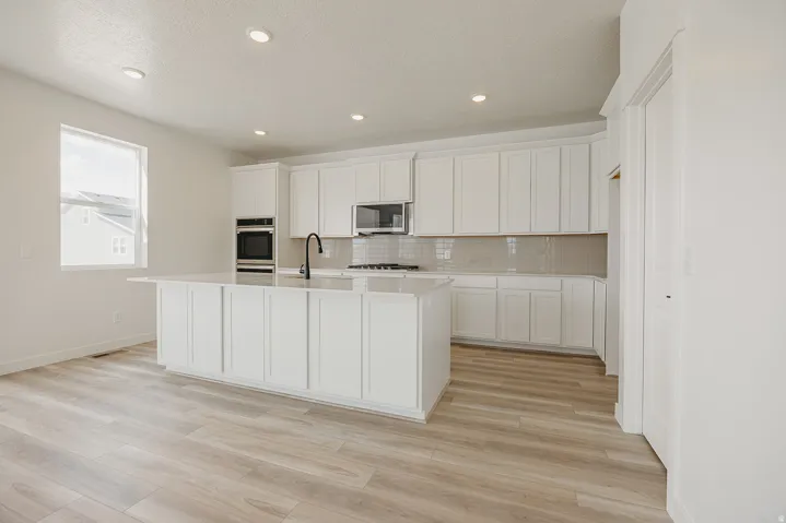 Kitchen featuring a center island, white cabinetry, integrated appliances, light-toned wood-finish flooring, and recessed lighting