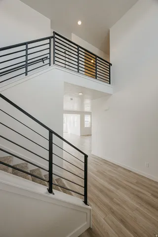 Open-concept entry with wood-finish flooring, a carpeted staircase featuring a black metal railing, and a second-level landing