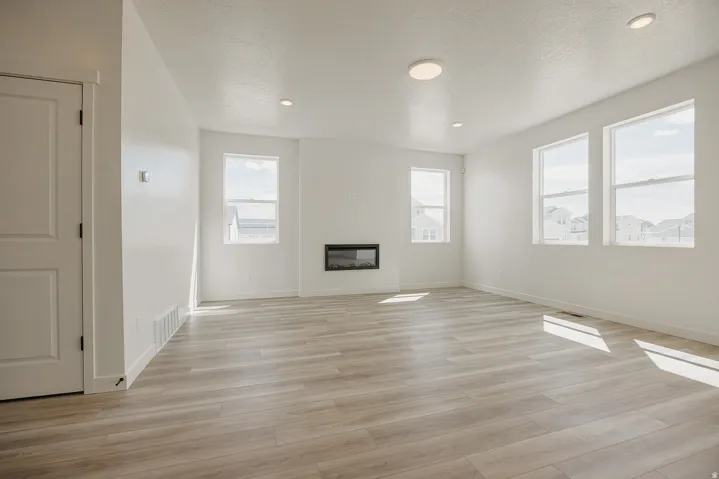 Spacious living area featuring light wood-finish flooring, recessed lighting, an electric fireplace, and multiple windows