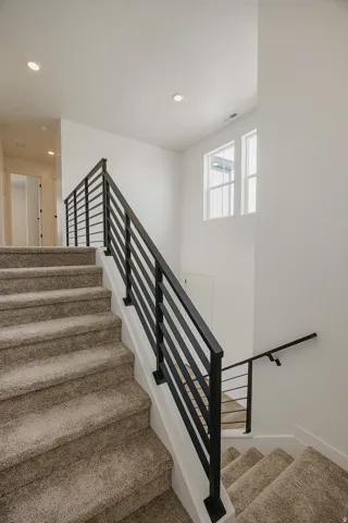 Carpeted staircase with contemporary black metal railings, recessed lighting, and upper-level windows
