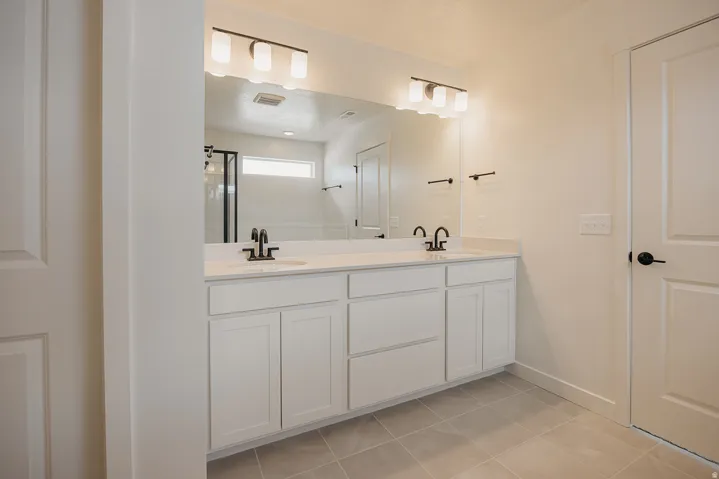 Dual vanity with white cabinetry, integrated sinks, black fixtures, and a large mirror with overhead lighting