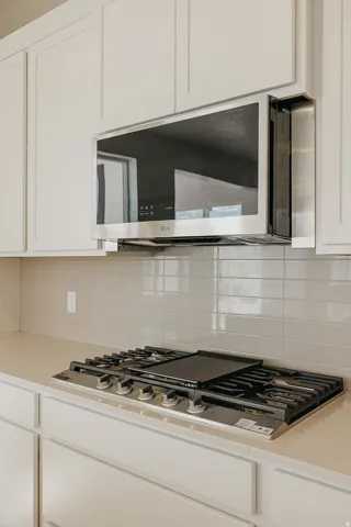 White shaker-style cabinetry, a stainless steel over-the-range microwave, a gas cooktop with griddle, light-toned countertops, and a subway tile backsplash
