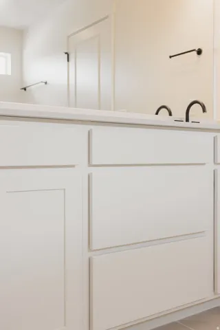 White vanity with shaker-style cabinetry, a light-toned countertop, and dual matte black faucets