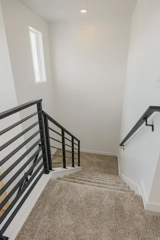 Staircase featuring carpeted treads, metal balusters, and a wall-mounted handrail