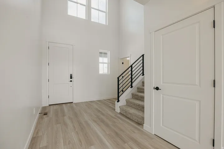 Two-story entry with wood-finish flooring, high ceilings, and an open staircase with a black metal railing