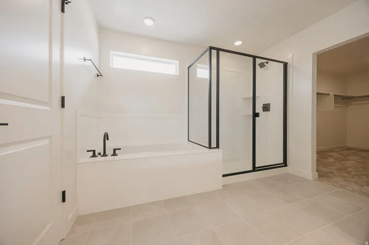 Recessed lighting, tile flooring, built-in soaking tub with matte black fixtures, and a glass-enclosed shower with matte black framing
