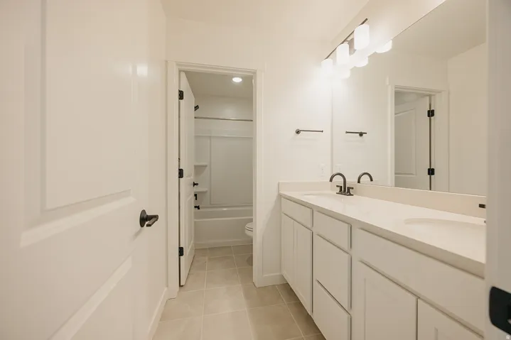 Dual vanity with undermount sinks, stone-look countertop, dark bronze fixtures, and overhead light bar