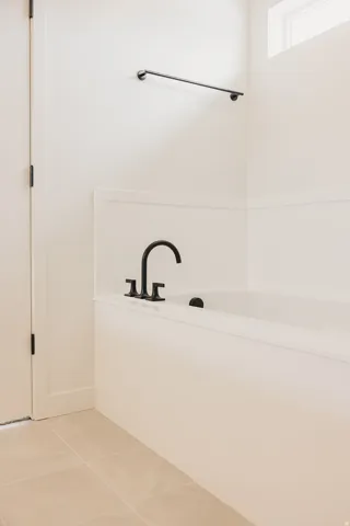 Integrated soaking tub with matte black fixtures, tile flooring, and a wall-mounted towel bar