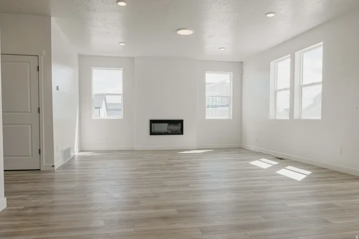 Spacious living area featuring wood-finish flooring, recessed lighting, multiple windows, and a built-in electric fireplace