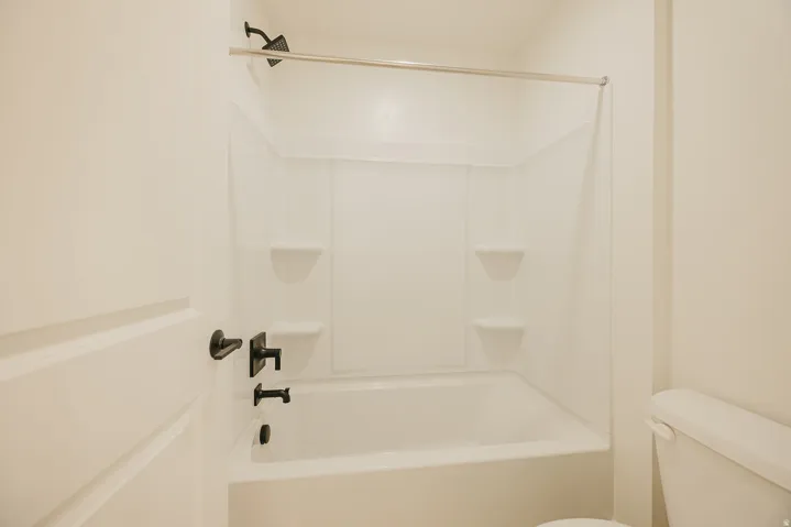 White acrylic tub and shower combination with integrated shelving, featuring matte black fixtures and a shower curtain rod