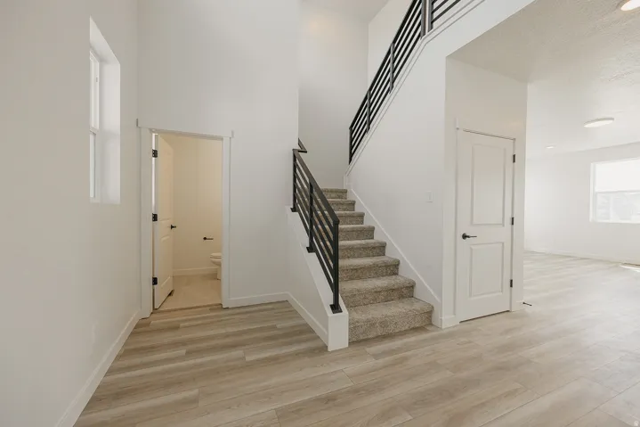 Two-story entry featuring light wood-finish flooring, a carpeted staircase with modern black metal railings, and a prominent window