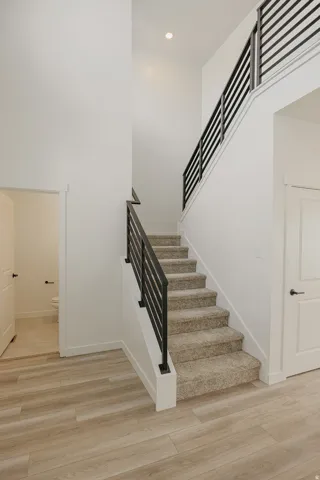High ceilings with recessed lighting, modern horizontal black metal stair railing, carpeted staircase, and wood-finish flooring