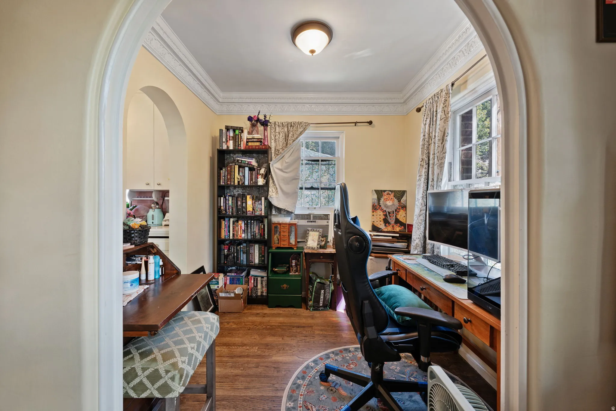 Archway entry leading to a room with wood-finish flooring, crown molding, and multiple windows