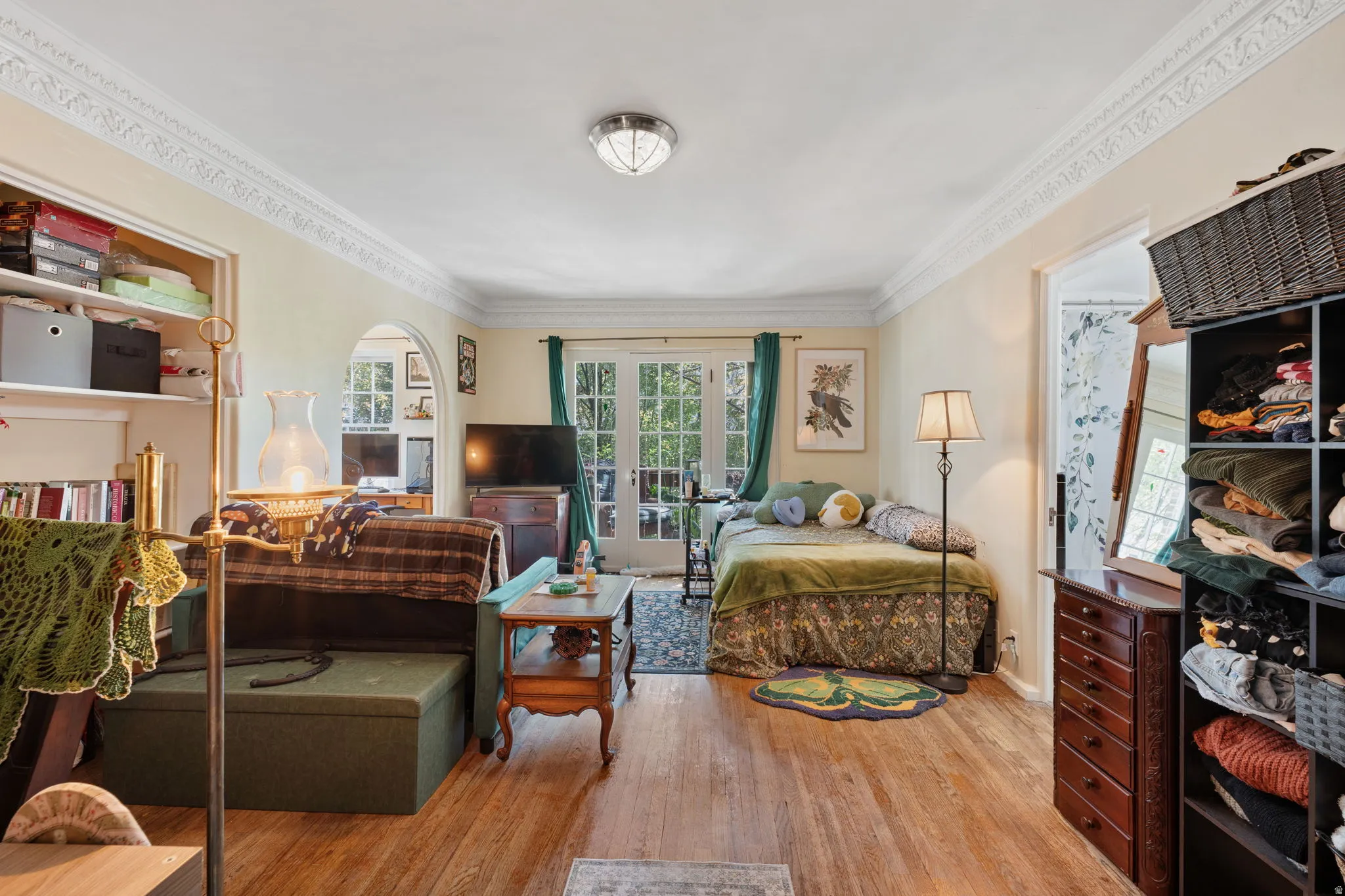Hardwood-style flooring throughout, detailed crown molding, built-in shelving, arched doorway, and French doors