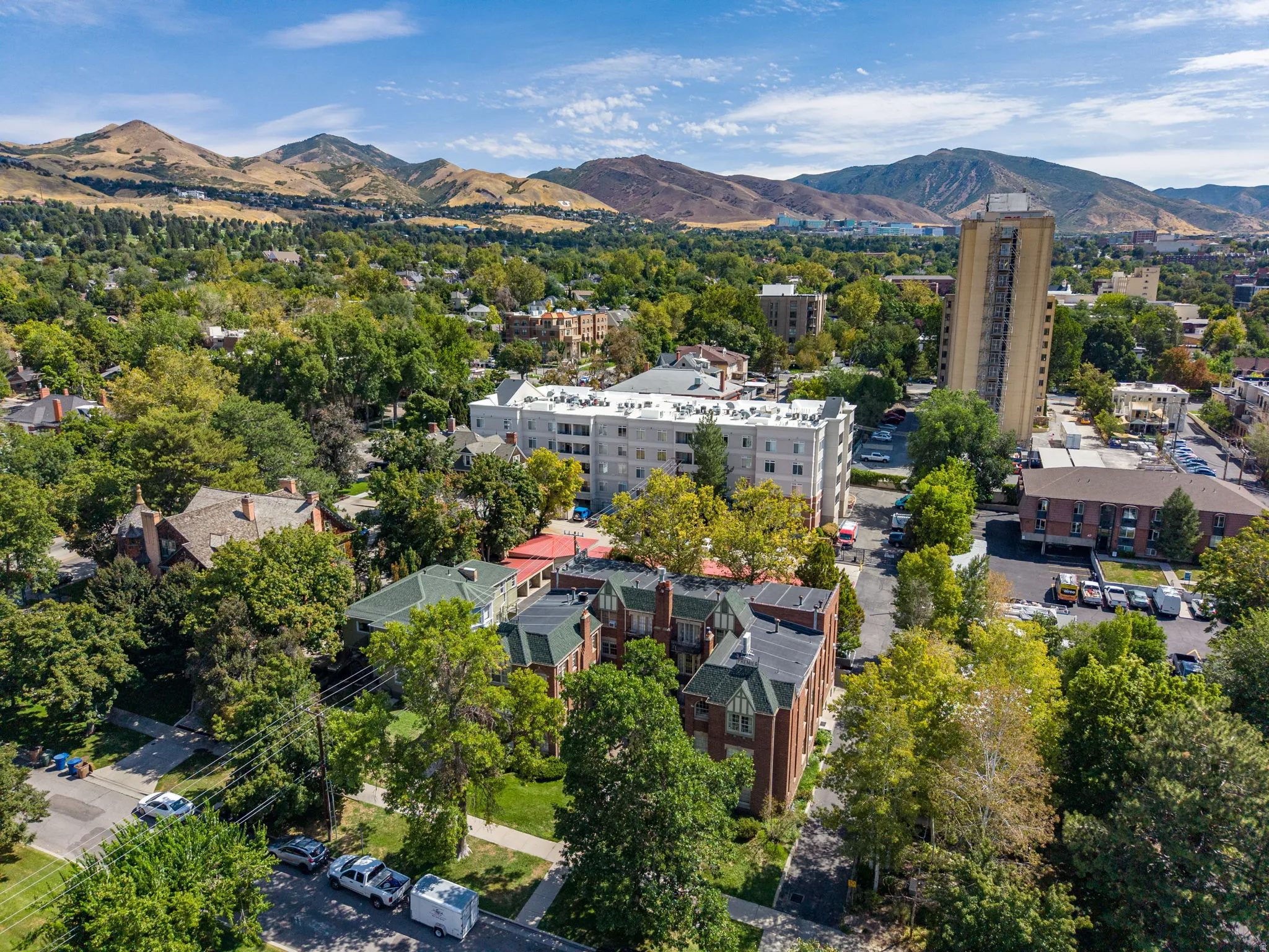 Expansive urban landscape featuring dense tree cover, multiple multi-story structures, and distant mountains