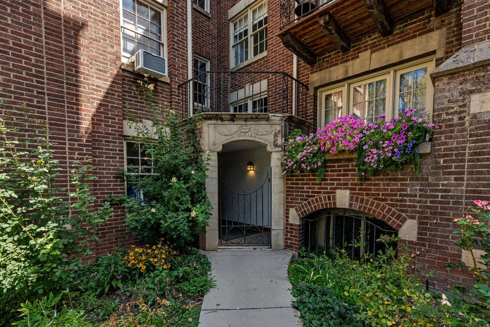 Brick facade with decorative stone accents, arched entryway with an iron gate, multiple windows, and a window box with colorful plantings
