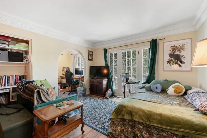 White crown molding, built-in shelving, arched doorway, French doors, and wood-finish flooring