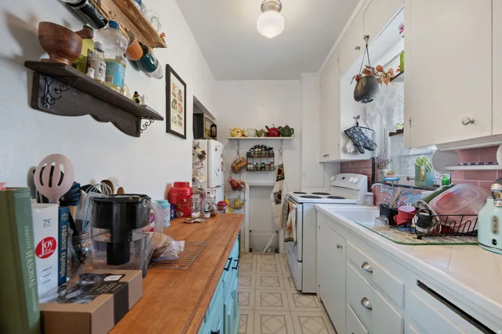 White cabinetry and appliances, wood-finish countertop, tile backsplash, and patterned flooring