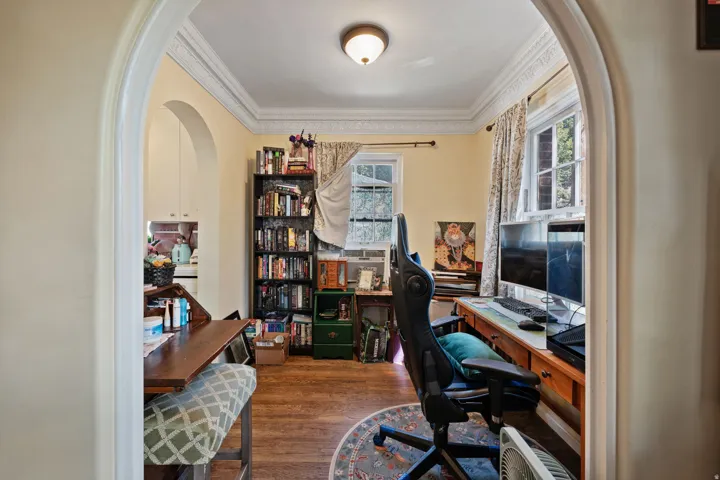Archway entry leading to a room with wood-finish flooring, crown molding, and multiple windows