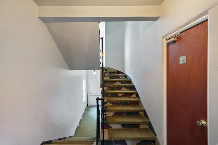 Staircase featuring patterned risers, a dark metal handrail, and a solid wood door with brass hardware
