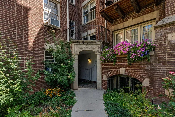 Brick facade with decorative stone accents, arched entryway with an iron gate, multiple windows, and a window box with colorful plantings