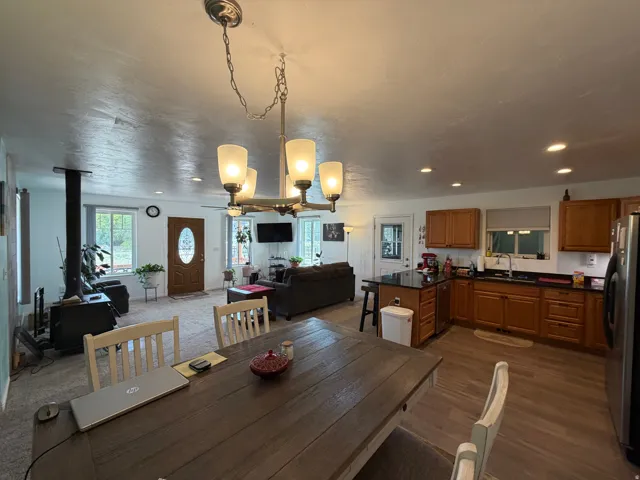 Open-concept living space featuring a wood-burning stove, a kitchen island with seating, wood-finish flooring, and recessed lighting