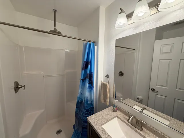 Bathroom featuring a shower with a ceiling-mounted rainfall showerhead, a shower/tub combination, a vanity with an integrated sink, a vanity mirror, and a three-light fixture